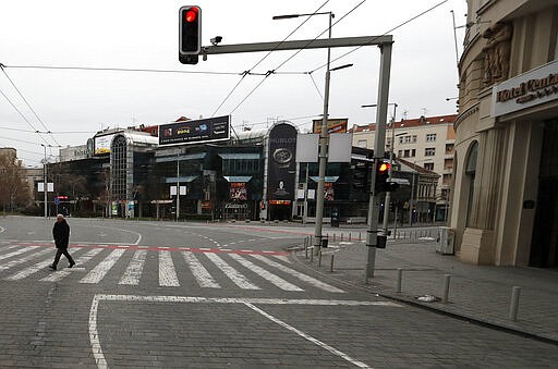 In this March 26, 2020, photo, a man walks on an empty main square during a curfew set up to help prevent the spread of the new coronavirus in Belgrade, Serbia. Since declaring nationwide state of emergency Serbian President Aleksandar Vucic has suspended parliament, giving him widespread powers such as closing borders and introducing a 12-hour curfew. (AP Photo/Darko Vojinovic)