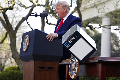 President Donald Trump speaks as a box containing a 5-minute test for COVID-19 from Abbott Laboratories blows off a table about the coronavirus in the Rose Garden of the White House, Monday, March 30, 2020, in Washington. (AP Photo/Alex Brandon)