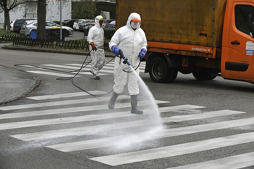 Municipal workers wearing protective clothing spray disinfectant on the streets to prevent the spread of the coronavirus in Budapest, Hungary, Monday, March 30, 2020. The new coronavirus causes mild or moderate symptoms for most people, but for some, especially older adults and people with existing health problems, it can cause more severe illness or death. (Zoltan Mihadak/MTI via AP)