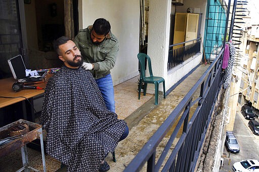 Barber Fouad Lalo cuts hair on the balcony of a customer's home, in Beirut, Lebanon, Thursday, March 26, 2020. Lebanon has been under a government-ordered lockdown since last week in an effort to stem the spread of the coronavirus. (AP Photo/Bilal Hussein)