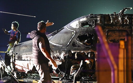 CORRECTS AIRLINE - An airport personnel walks beside the remains of a Lionair, West Wind 24 aircraft after it caught fire during take off at Manila's International Airport in Philippines on Sunday, March 29, 2020. A plane carrying eight people has caught fire while attempting to take off from Manila's airport on a flight bound for Japan, killing all those on board, officials said. (AP Photo)