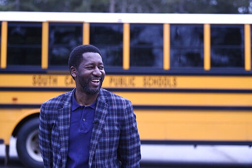 In this Thursday, March 26, 2020, photo, Fairfield County Schools Superintendent J.R. Green stands in front of a wi-fi-enabled school bus in Winnsboro, S.C. The bus is one of many being sent to rural and lower-income areas around South Carolina to help students with distance learning during the new coronavirus outbreak. With routers mounted inside, the buses broadcast enough bandwidth in an area the size of a small parking for parents to drive up and children to access the internet from inside their cars. (AP Photo/Meg Kinnard)