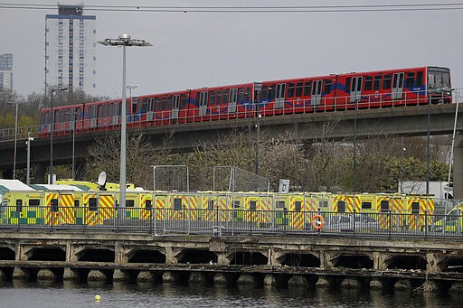 A line of London ambulances outside the ExCel center, which is being turned into a 4000 bed temporary hospital called NHS Nightingale to deal with coronavirus patients, as a train passes by in London, Monday, March 30, 2020. The new coronavirus causes mild or moderate symptoms for most people, but for some, especially older adults and people with existing health problems, it can cause more severe illness or death.(AP Photo/Matt Dunham)