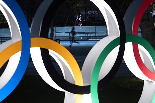 A man jogs past the Olympic rings Monday, March 30, 2020, in Tokyo. The Tokyo Olympics will open next year in the same time slot scheduled for this year's games. Tokyo organizers said Monday the opening ceremony will take place on July 23, 2021. (AP Photo/Jae C. Hong)