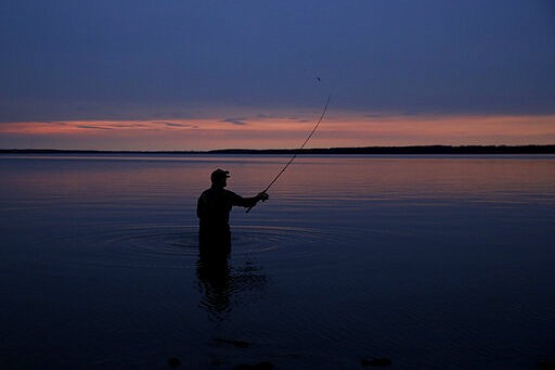 A man is silhouetted at dusk as he practices the solitary pastime of fishing on the first day of a stay-at-home order Monday, March 30, 2020 at Hillsdale Lake near Hillsdale, Kan. The statewide order was the latest measure enacted by Kansas Gov. Laura Kelly in an attempt to curb the spread of the new coronavirus. (AP Photo/Charlie Riedel)