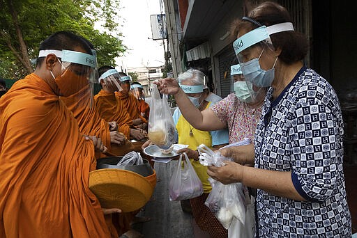 Devotees offer food to Thai Buddhist monks as they wear face shield to protect themselves from new coronavirus in Bangkok, Thailand, Tuesday, March 31, 2020. The new coronavirus causes mild or moderate symptoms for most people, but for some, especially older adults and people with existing health problems, it can cause more severe illness or death. (AP Photo/Sakchai Lalit)