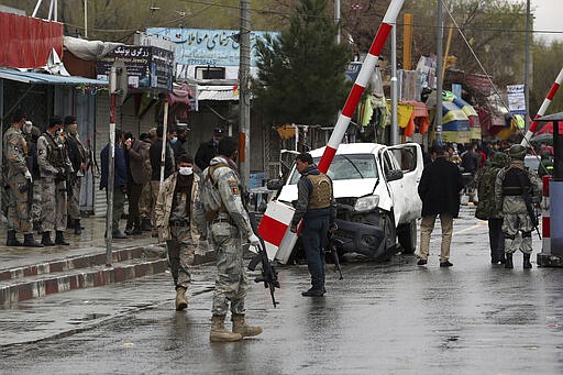 Afghan security forces inspect the site of a bomb explosion near a damaged vehicle in Kabul, Afghanistan, Monday, March 30, 2020.  A sticky bomb attached to the vehicle detonated, according to Firdaus Faramraz, spokesman for the Kabul police chief. (AP Photo/Rahmat Gul)