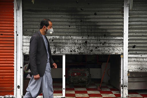 An Afghan man wearing a face mask walks in front of a damaged shop after a bomb explosion in Kabul, Afghanistan, Monday, March 30, 2020. A sticky bomb attached to a vehicle detonated, according to Firdaus Faramraz, spokesman for the Kabul police chief. (AP Photo/Rahmat Gul)