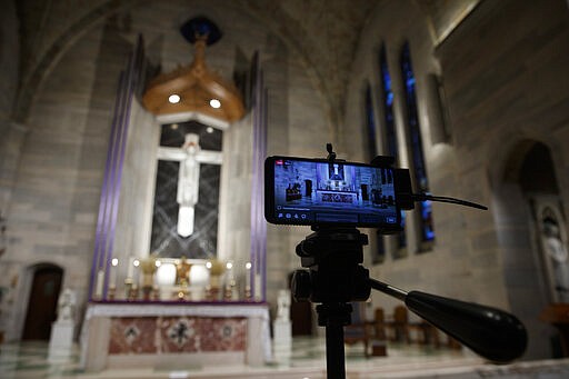 A smartphone is used to livestream a Eucharistic Adoration service at Saint Ann Catholic Church in Washington, Sunday night, March 29, 2020. The Archdiocese of Washington has temporarily halted all public Masses and gatherings in an effort to contain the spread of the coronavirus. This service was live streamed and those few who attended practiced social distancing. During Eucharistic Adoration the Blessed Sacrament is exposed, with the white Host visible within a golden display case called a monstrance. (AP Photo/Carolyn Kaster)