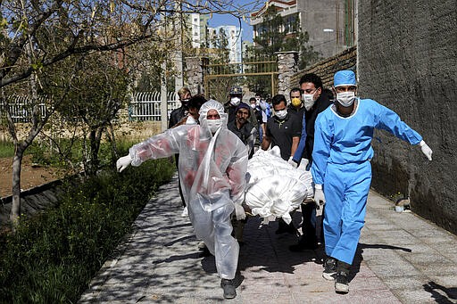 People wearing protective clothing carry the body of a victim who died after being infected with the new coronavirus at a cemetery just outside Tehran, Iran, Monday, March 30, 2020. The new coronavirus causes mild or moderate symptoms for most people, but for some, especially older adults and people with existing health problems, it can cause more severe illness or death. (AP Photo/Ebrahim Noroozi)