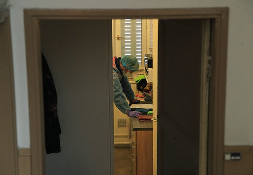 In this photo taken Saturday March 28, 2020, Cyril Lamriben, a member of the Civil Protection service checks a document as he takes care of a woman possibly infected with the Covid-19 virus in Paris. The Civil Protection service is a mainstay among France's first responder sector with 32,000 volunteers based in 400 locations around the country. (AP Photo/Michel Euler)