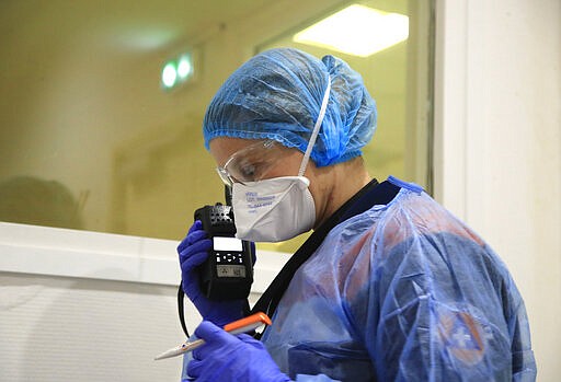 In this photo taken Thursday, March 26, 2020 Aurore Lejeune, a member of the Civil Protection service, checks a thermometer as she talks to a doctor on a talkie-wakie in Paris. Lejeune is in her 14th year volunteering for Civil Protection, but she says she hasn't encountered such high-risk situations in the past. (AP Photo/Michel Euler)