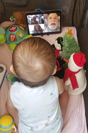 In this March 23, 2020, photo provided by Julie Bufkin, her 7-month-old boy, Calvin, interacts with his grandparents, Debbie and Allan Cameron, in Chandler, Ariz., on a FaceTime video call from his crib in Tempe, Ariz. The Camerons are among the grandparents all over the country going through a piercing distance from their loved ones for their own protection during the coronavirus crisis. (Julie Bufkin via AP)