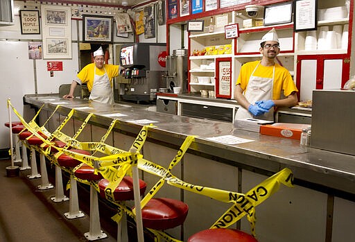 Texas Tavern employees Chris Dobe, left, and Nick Moore wait for take out orders on Monday night, March 30, 2020. Though customers are tipping well, and the diner is still open 24-7, Moore said they are making a quarter to a third less than what they normally do in tips. (Heather Rousseau/The Roanoke Times via AP)