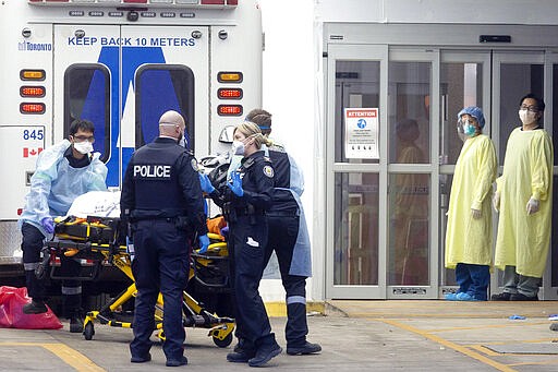 Hospital staff dressed in protective equipment stand by as a patient is taken out of an ambulance at Toronto's Mount Sinai Hospital, Sunday, March 29, 2020. The new coronavirus causes mild or moderate symptoms for most people, but for some, especially older adults and people with existing health problems, it can cause more severe illness or death. (Chris Young/The Canadian Press via AP)