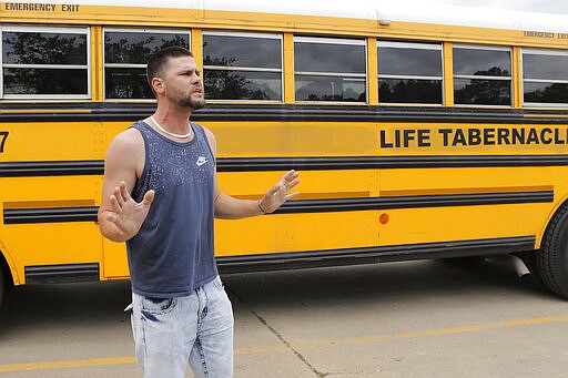 Passer-by Ryan Tregre expresses his displeasure with the Life Tabernacle Church as church buses transport congregants after services in Central, La., Sunday, March 29, 2020. Pastor Tony Spell has defied a shelter-in-place order by Louisiana Gov. John Bel Edwards, due to the new coronavirus pandemic, and continues to hold church services with hundreds of congregants. (AP Photo/Gerald Herbert)