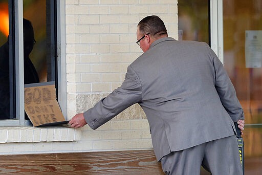 A man removes a sign left behind by a protestor that reads &quot;God don't like stupid,&quot; as congregants arrive for evening service at the Life Tabernacle Church in Central, La., Tuesday, March 31, 2020. Pastor Tony Spell held services despite being charged with misdemeanors today, for holding services against Gov. John Bel Edwards shelter-in-place order due to the new coronavirus pandemic. (AP Photo/Gerald Herbert)