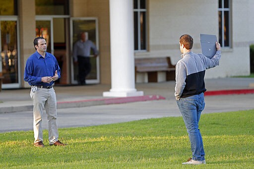 A man questions a lone protestor as congregants arrive for evening service at the Life Tabernacle Church in Central, La., Tuesday, March 31, 2020. Pastor Tony Spell held services despite being charged with misdemeanors today, for holding services against Gov. John Bel Edwards shelter-in-place order due to the new coronavirus pandemic. (AP Photo/Gerald Herbert)