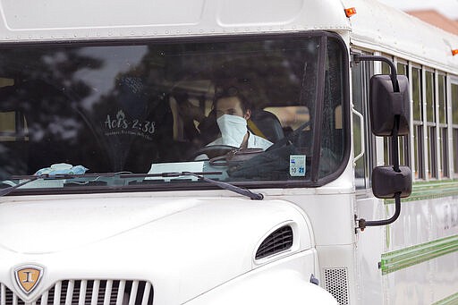 A church bus driver wears a mask as he drives congregants after services at the Life Tabernacle Church in Central, La., Sunday, March 29, 2020. Pastor Tony Spell has defied a shelter-in-place order by Louisiana Gov. John Bel Edwards, due to the new coronavirus pandemic, and continues to hold church services with hundreds of congregants. (AP Photo/Gerald Herbert)