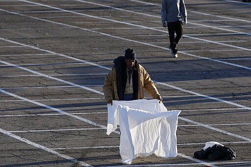 People prepare places to sleep in areas marked by painted boxes on the ground of a parking lot at a makeshift camp for the homeless Monday, March 30, 2020, in Las Vegas. Officials opened part of the lot as a makeshift homeless shelter after a local shelter closed when a man staying there tested positive for the coronavirus. (AP Photo/John Locher)