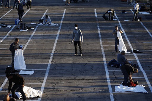 People prepare to sleep in areas marked by painted boxes on the ground of a parking lot at a makeshift camp for the homeless Monday, March 30, 2020, in Las Vegas. Officials opened part of the lot as a makeshift homeless shelter after a local shelter closed when a man staying there tested positive for coronavirus. (AP Photo/John Locher)