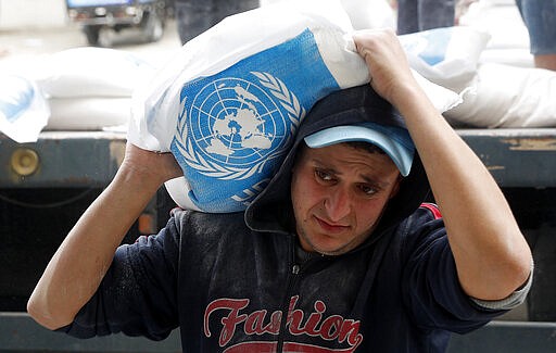 A Palestinian worker carries sacks of flour distributed by the United Nations Relief and Works Agency (UNRWA) for poor refugee families, at the Sheikh Redwan neighborhood of Gaza City, Tuesday, March 31, 2020. The United Nations has resumed food deliveries to thousands of impoverished families in the Gaza Strip after a three-week delay caused by fears of the coronavirus. UNRWA, provides staples like flour, rice, oil and canned foods to roughly half of Gaza&#146;s 2 million people. (AP Photo/Adel Hana)