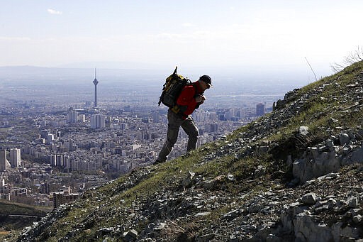 A hiker ascend a foothill of the Alborz mountain range, overlooking the capital Tehran, as he spends his New Year, or Nowruz, holidays, Iran, Tuesday, March 31, 2020. In recent days, Iran which is battling the worst new coronavirus outbreak in the region, has ordered the closure of nonessential businesses and banned intercity travels aimed at preventing the virus' spread. Public parks are closed as well as sport and recreational clubs which were shut previously. (AP Photo/Vahid Salemi)