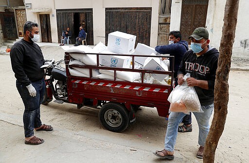 Palestinian workers distribute food supplies from the United Nations Relief and Works Agency (UNRWA) for impoverished refugee families after a three-week delay caused by fears of the coronavirus, in the Sheikh Redwan neighborhood of Gaza City, Tuesday, March 31, 2020. Gaza, which is blockaded by its neighbors Israel and Egypt, has only detected a few cases of coronavirus, with all of them confined to quarantine centers. But international officials fear the virus could quickly spread in the densely populated area, whose overburdened health system is not equipped to deal with a large outbreak. (AP Photo/Adel Hana)