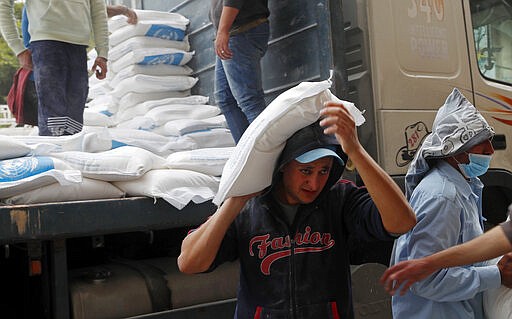 Palestinian workers unloads sacks of flour distributed by the United Nations Relief and Works Agency (UNRWA) for poor refugee families, at the Sheikh Redwan neighborhood of Gaza City, Tuesday, March 31, 2020. The United Nations has resumed food deliveries to thousands of impoverished families in the Gaza Strip after a three-week delay caused by fears of the coronavirus. UNRWA, provides staples like flour, rice, oil and canned foods to roughly half of Gaza&#146;s 2 million people. (AP Photo/Adel Hana)