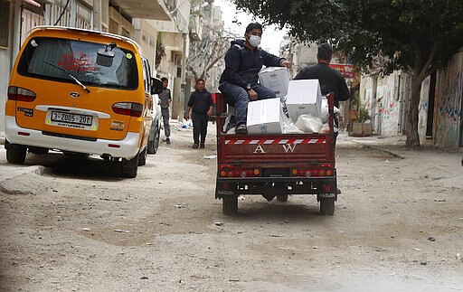 Palestinian workers distribute food supplies from the United Nations Relief and Works Agency (UNRWA) for impoverished refugee families after a three-week delay caused by fears of the coronavirus, at the Sheikh Redwan neighborhood of Gaza City, Tuesday, March 31, 2020. Gaza, which is blockaded by its neighbors Israel and Egypt, has only detected a few cases of coronavirus, with all of them confined to quarantine centers. But international officials fear the virus could quickly spread in the densely populated area, whose overburdened health system is not equipped to deal with a large outbreak. (AP Photo/Adel Hana)