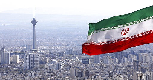 Iran's national flag waves as Milad telecommunications tower and buildings are seen in Tehran, Iran, Tuesday, March 31, 2020. In recent days, Iran which is battling the worst new coronavirus outbreak in the region, has ordered the closure of nonessential businesses and banned intercity travels aimed at preventing the virus' spread.   (AP Photo/Vahid Salemi)