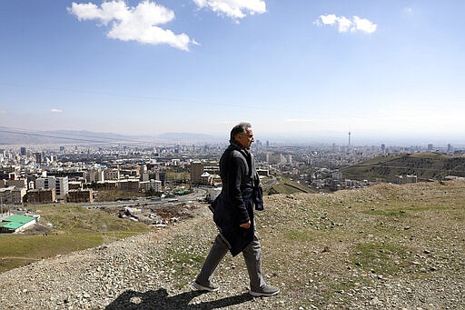 A man hikes in foothill of the Alborz mountain range, overlooking the capital Tehran, as he spends his New Year, or Nowruz, holidays, Iran, Tuesday, March 31, 2020. In recent days, Iran which is battling the worst new coronavirus outbreak in the region, has ordered the closure of nonessential businesses and banned intercity travels aimed at preventing the virus' spread. Public parks are closed as well as sport and recreational clubs which were shut previously. (AP Photo/Vahid Salemi)