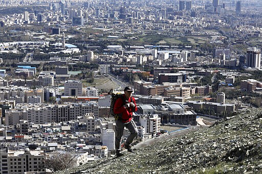 A hiker ascend a foothill of the Alborz mountain range, overlooking the capital Tehran, as he spends his New Year, or Nowruz, holidays, Iran, Tuesday, March 31, 2020. In recent days, Iran which is battling the worst new coronavirus outbreak in the region, has ordered the closure of nonessential businesses and banned intercity travels aimed at preventing the virus' spread.   (AP Photo/Vahid Salemi)