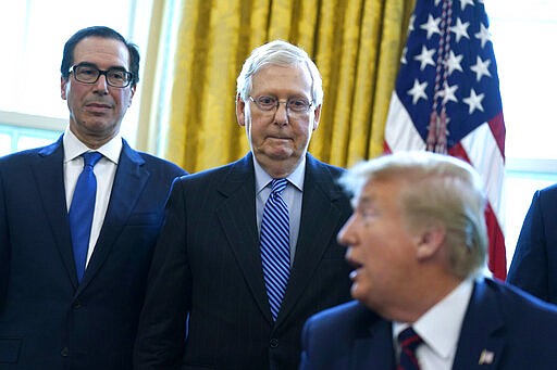 Treasury Secretary Steven Mnuchin and Senate Majority Leader Mitch McConnell, R-Ky., listen as President Donald Trump speaks before he signs the coronavirus stimulus relief package in the Oval Office at the White House, Friday, March 27, 2020, in Washington. (AP Photo/Evan Vucci)