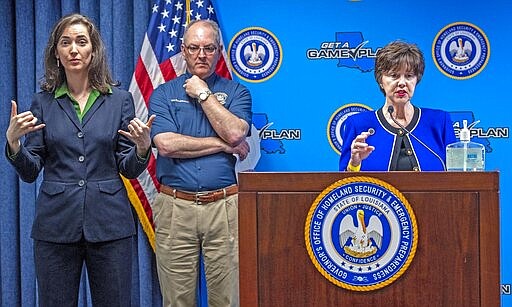 Observing social distancing, Gov. John Bel Edwards, center, watches as Louisiana Department of Children and Family Services Secretary Marketa Walters, right, addresses supplemental SNAP benefits in response to the coronavirus during a press conference at GOHSEP Monday March 30, 2020, in Baton Rouge, La. Sylvie Sullivan, left, does sigs interpretation for the meeting. (Bill Feig/The Advocate via AP, Pool)