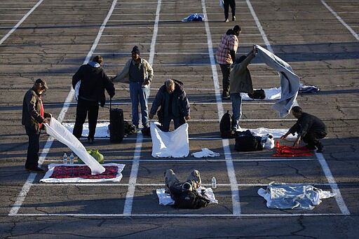 People prepare places to sleep in area marked by painted boxes on the ground of a parking lot at a makeshift camp for the homeless Monday, March 30, 2020, in Las Vegas. Officials opened part of a parking lot as a makeshift homeless shelter after a local shelter closed when a man staying there tested positive for the coronavirus. (AP Photo/John Locher)