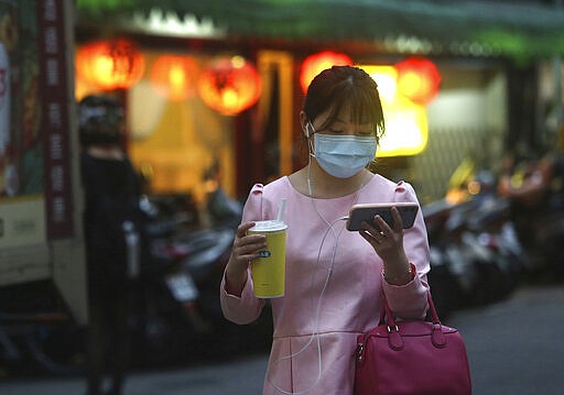 A woman her protective face mask balances her large-sized cup while watching her smart phone in Taipei, Taiwan, Tuesday, March 31, 2020. The new coronavirus causes mild or moderate symptoms for most people, but for some, especially older adults and people with existing health problems, it can cause more severe illness or death. (AP Photo/Chiang Ying-ying)