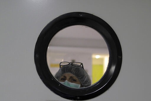 A health worker wearing a face mask to protect from coronavirus, looks out of from a window at a nursing home in Madrid, Spain, Tuesday, March 31, 2020. The new coronavirus causes mild or moderate symptoms for most people, but for some, especially older adults and people with existing health problems, it can cause more severe illness or death. (AP Photo/Manu Fernandez)