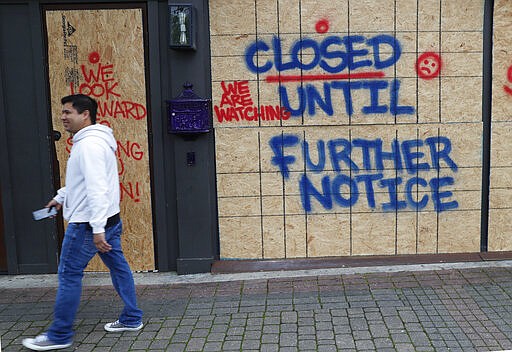 Eric Manzanares walks past a closed tattoo shop amid concerns of COVID-19 spreading in the Deep Ellum section of Dallas, Tuesday, March 31, 2020. For most people, the coronavirus causes mild or moderate symptoms, such as fever and cough that clear up in two to three weeks. For some, especially older adults and people with existing health problems, it can cause more severe illness, including pneumonia and death. (AP Photo/LM Otero)