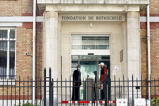 In this photo taken on Friday March 27, 2020 men wearing face masks chat at the entrance of the Fondation Rothschild nursing home, in Paris. Governments in Europe's hardest-hit countries have yet to systematically test the residents of nursing homes or those who receive in-home care. In Spain, Italy and France, which together account for a third of the world's confirmed coronavirus cases, no one knows for sure how many people have become sick and died of coronavirus, especially among the elderly. The new coronavirus causes mild or moderate symptoms for most people, but for some, especially older adults and people with existing health problems, it can cause more severe illness or death. (AP Photo/Thibault Camus)