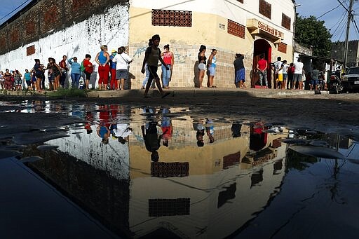 Neighbors line up for free food staples outside Santa Ana primary school in Asuncion, Paraguay, Tuesday, March 31, 2020, part of an already existing food program through the Education Ministry, as people stay home from work amid the spread of the new coronavirus. COVID-19 causes mild or moderate symptoms for most people, but for some, especially older adults and people with existing health problems, it can cause more severe illness or death. (AP Photo/Jorge Saenz)