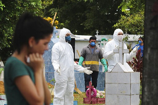 Funeral and cemetery workers pray next to the grave of Robson de Souza Lopes after burying him as a relative stands at a distance inside the Parque Taruma cemetery in Manaus, Brazil, Tuesday, March 31, 2020. According to authorities at the Amazonas Health Secretary, the 43-year-old musician died Monday after being diagnosed with COVID-19. (AP Photo/Edmar Barros)