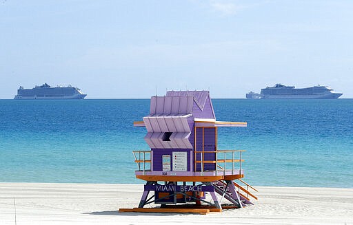 Two cruise ships are anchored offshore past a lifeguard tower, Tuesday, March 31, 2020, in Miami Beach, Fla. (AP Photo/Wilfredo Lee)