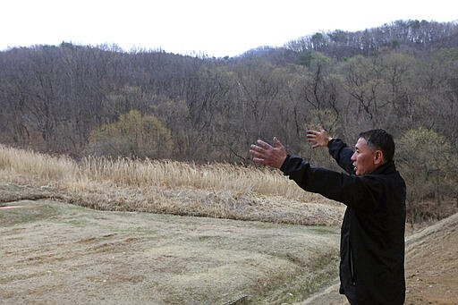 In this March 25, 2020 photo, South Korean shoe repairman Kim Byung-rok speaks in front of his land during an interview in Paju, South Korea. Kim is in news after he revealed plans to donate his property to help support people facing economic difficulties amid the coronavirus outbreak. Kim says he wants to donate parts of his land on a small mountain near the border with North Korea that he bought in 2014.(AP Photo/Ahn Young-joon)