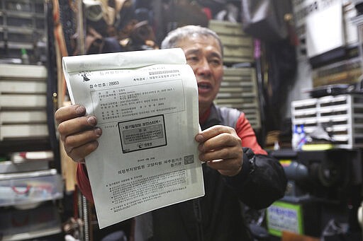 In this March 25, 2020 photo, South Korean shoe repairman Kim Byung-rok holds his land ownership registration documents during an interview at his shop in Seoul, South Korea. Kim is in news after he revealed plans to donate his property to help support people facing economic difficulties amid the coronavirus outbreak. Kim says he wants to donate parts of his land on a small mountain near the border with North Korea that he bought in 2014. (AP Photo/Ahn Young-joon)