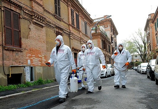 Workers wearing protective outfits sanitize a neighborhood to contain the spread of Covid-19 virus, in Rome,  Saturday, March 28, 2020. The new coronavirus causes mild or moderate symptoms for most people, but for some, especially older adults and people with existing health problems, it can cause more severe illness or death. (Mauro Scrobogna/LaPresse via AP)