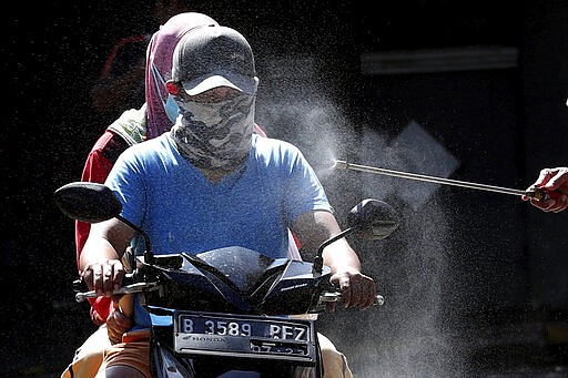 Motorists are sprayed with disinfectant in an attempt to curb the spread of coronavirus outbreak at the gate of a housing complex in South Tangerang, Indonesia, Tuesday, March 31, 2020. Indonesia will close its doors to foreign arrivals in an attempt to curb the coronavirus spread while the country plans to bring home more than a million nationals working abroad. (AP Photo/Tatan Syuflana)