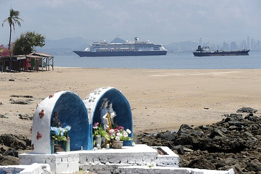 The Zaandam cruise ship, top center, carrying dozens of guests with flu-like symptoms, arrives to the bay of Panama City, seen from Isla de Taboga, Panama, Friday, March 27, 2020, amid the worldwide spread of the new coronavirus. Once the vessel reaches Panamanian waters, health authorities are expected to board the ship to test passengers and decide whether it can cross the Panama Canal to head on towards Fort Lauderdale. On the beach in the foreground is a Catholic altar featuring Our Lady of Mount Carmel, or &quot;La Virgen del Carmen,&quot; considered the patron saint of sailors. (AP Photo/Arnulfo Franco)