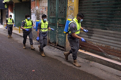 In this Friday, March 27, 2020 photo, members of the Islamic Health Society, an arm of the Iran-backed militant Hezbollah group spray disinfectant as a precaution against the coronavirus, in a southern suburb of Beirut, Lebanon. Hezbollah has mobilized the organizational might it once deployed to fight Israel or in Syria's civil war to battle the spread of the novel coronavirus. It aims to send a clear message to its Shiite supporters that it is a force to rely on in times of crisis -- particularly after it suffered a series of blows to its prestige. Opponents angrily accuse Hezbollah of helping bring the outbreak to Lebanon, saying it delayed a halt of flights from Iran for weeks after a woman who had just arrived from Iran emerged as Lebanon's first confirmed coronavirus case. (AP Photo/Bilal Hussein)