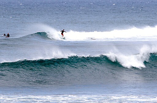 A surfer rides a wave on Oahu's North Shore near Haleiwa, Hawaii, Tuesday, March 31, 2020. Hawaii Gov. David Ige is further tightening travel restrictions to limit the spread of the coronavirus by ordering people moving between islands to adhere to a 14-day self-quarantine. The order takes effect at midnight on Wednesday. It won't apply to essential workers like health care workers traveling to other islands. He's also ordered everyone in the state to stay at home for the next month. (AP Photo/Caleb Jones)